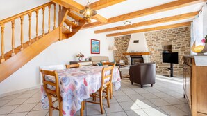 A dining area with a wooden staircase, a stone fireplace, and a television.