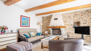 A living room with a stone fireplace, a sofa, a television, and a wooden ceiling.