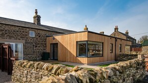 A modern house with a stone exterior, a wooden extension, and a stone wall in front. - Lakeside Cottage, Emily in Capheaton, Northumberland - sleeping 2 guests in one bedroom (Capheaton)