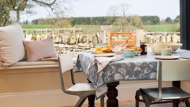 A table set with breakfast items, a stone wall, and a view of the countryside. - Lakeside Cottage, Emily in Capheaton, Northumberland - sleeping 2 guests in one bedroom (Capheaton)