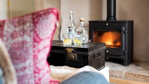 A cozy living room with a fireplace, a vintage suitcase, and a glass of water on a table. - Lakeside Cottage, Emily in Capheaton, Northumberland - sleeping 2 guests in one bedroom (Capheaton)
