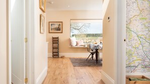 A hallway with wooden flooring, a window seat with a table, framed artwork, and a map on the wall. - Lakeside Cottage, Emily in Capheaton, Northumberland - sleeping 2 guests in one bedroom (Capheaton)