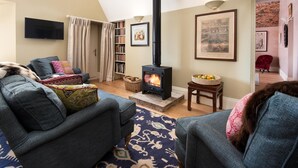 A cozy living room with a fireplace, comfortable seating, a bookshelf, and a flat-screen TV.