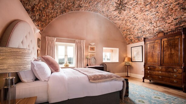A bedroom with a large bed, a wooden wardrobe, a nightstand, a lamp, and a window with curtains.