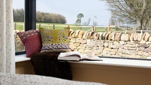 A window seat with a stone wall, a book, and two patterned cushions.
