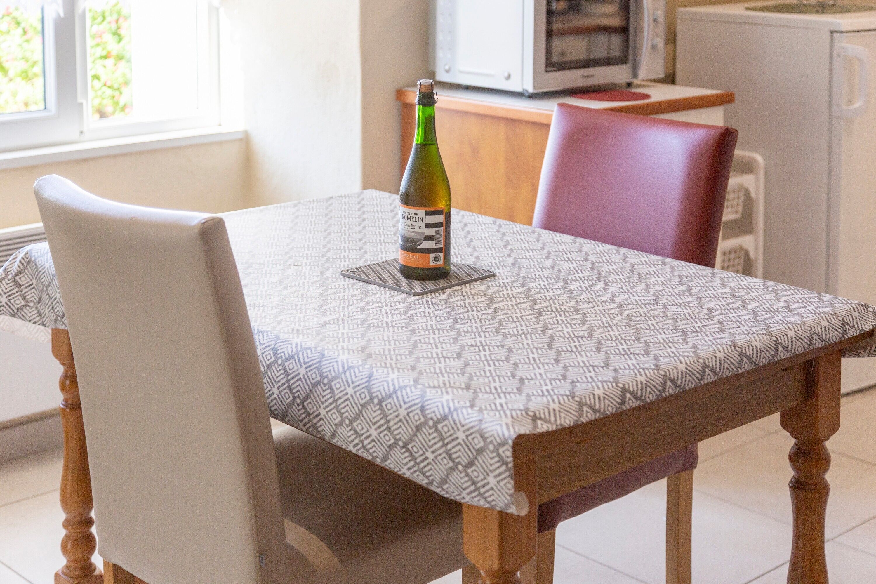 Une table à manger avec une bouteille de vin, une nappe à motifs et une chaise.