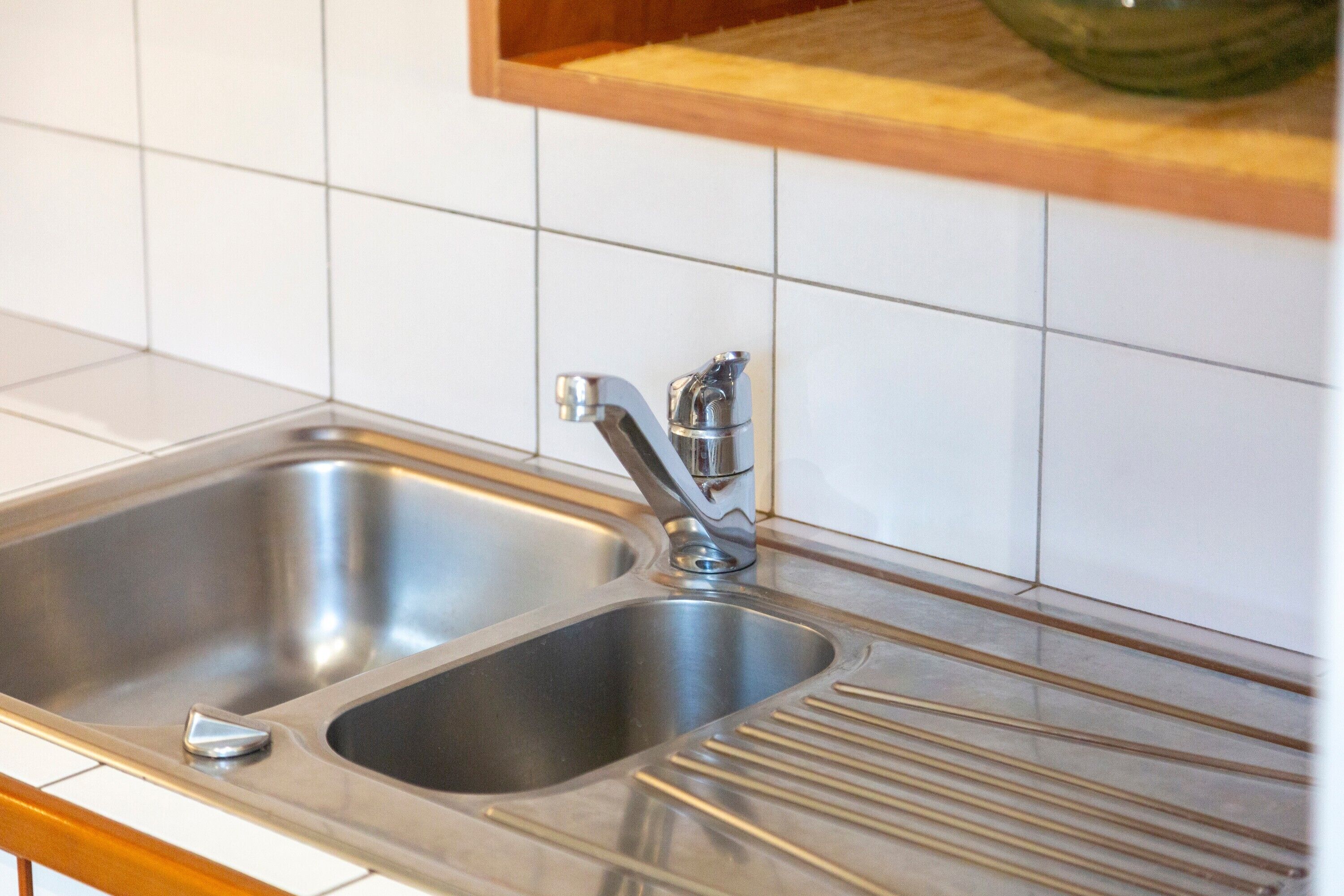 Een rvs spoelbak met een enkele kraan, een houten aanrechtblad en een witte betegelde achterwand.