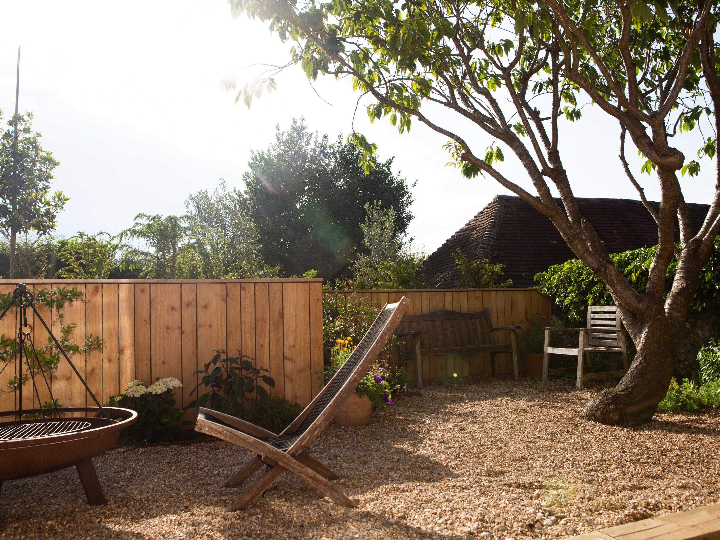A wooden deck with a metal grill, a wooden chair, and a tree.