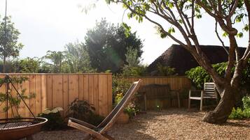 A wooden deck with a metal grill, a wooden chair, and a tree.