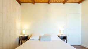 A bed with white linens, two bedside tables with lamps, a wooden headboard, and a white door. - Gîte Glycine, Kerantum: Shared Garden and Wi-Fi in Mahalon (Mahalon)