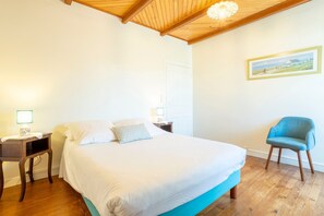 A bedroom with a bed, bedside tables, a chair, wooden flooring, and a wooden ceiling.
