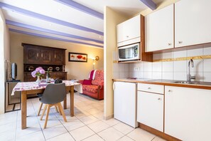 A compact kitchen with white cabinets, a microwave, and a sink. There is a dining area with a table and chairs, and a sofa in the background.