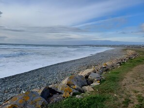 A rocky shoreline with waves, a clear sky, and distant land.