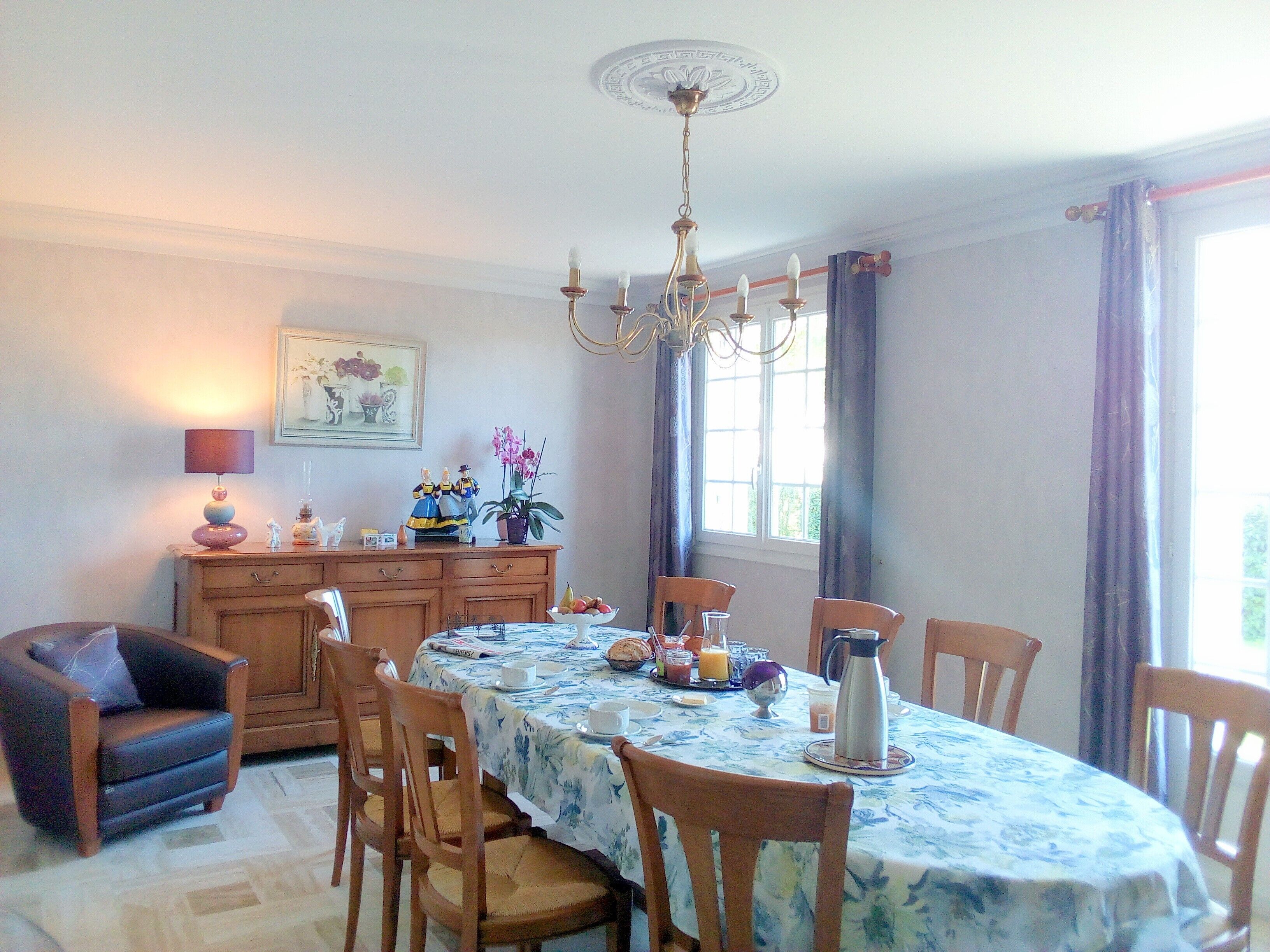 A dining area with a table set for four, chairs, a chandelier, a cabinet with decorative items, and a window with curtains.