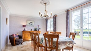 Ein Essbereich mit einem Tisch, gedeckt für sechs Personen, Holzstühlen, einer Chandelierleuchtre und Blick durch große Fenster.