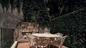 Une terrasse extérieure avec une table ronde et des chaises, entourée d’une végétation luxuriante et d’un mur de pierre orné d’une sculpture en relief.