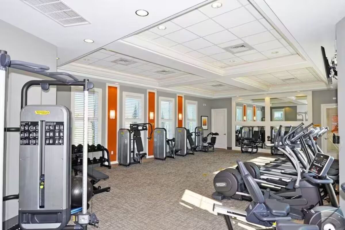 A gym with various exercise machines, a mirrored wall, and a carpeted floor.