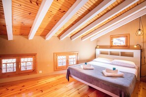 A bedroom with a wooden ceiling, a bed with a grey bedspread, two windows, and a wall-mounted picture. - Sabetche - baskeyrentals (Lekeitio)