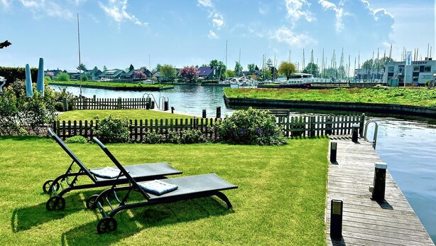 A riverside view with a grassy area, a wooden dock, and a row of houses in the background. - Stunning home in Lemmer with WiFi (Lemmer)