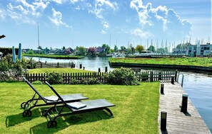 A riverside view with a grassy area, a wooden dock, and a row of houses in the background. - Stunning home in Lemmer with WiFi (Lemmer)