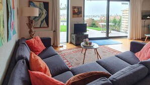 A living room with a large sofa, a small table, and a television. There are paintings on the wall and a view of the outdoors through the windows. - Stunning home in Lemmer with WiFi (Lemmer)