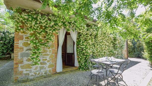 A stone building with a brick entrance, a covered patio with metal chairs, and a lush green vine-covered wall.