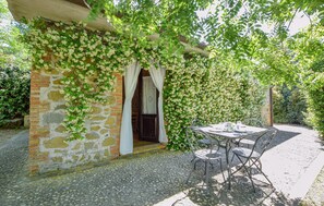 A stone building with a brick entrance, a covered patio with metal chairs, and a lush green vine-covered wall. - Amazing home in San Vito in Monte (San Vito in Monte)
