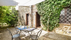 A stone building with ivy-covered walls, a metal table with chairs, and a small garden area. - Amazing apartment in San Vito in Monte (San Vito in Monte)