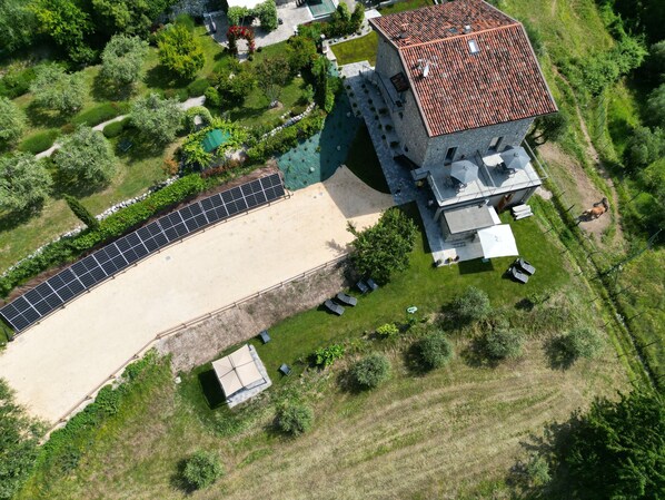 Vista aérea de una propiedad con una piscina grande, una zona de estar al aire libre techada y un edificio de piedra con techo de tejas.