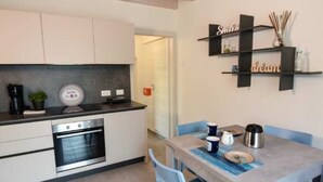 Una cocina compacta con horno empotrado, una mesa de comedor con sillas, y una estantería con adornos.