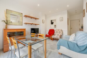 Un salon moderne avec une table à manger en verre, des chaises en bois, un fauteuil rouge, un canapé, un téléviseur et une cheminée.
