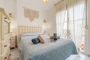 Une chambre à coucher avec un lit, des tables de chevet, une décoration murale en macramé et une fenêtre avec des rideaux.