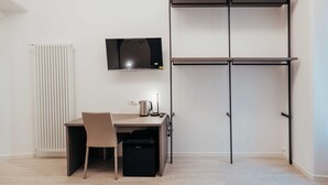 Una habitación minimalista con escritorio, silla, radiador, televisor y estantería.