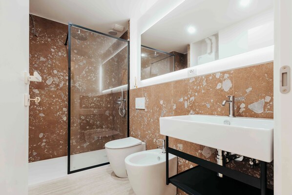 Een moderne badkamer met een glazen douchecabine, toilet en wastafel.
