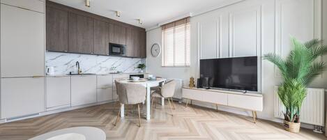 A modern kitchen with a dining area, a TV, and a potted plant.