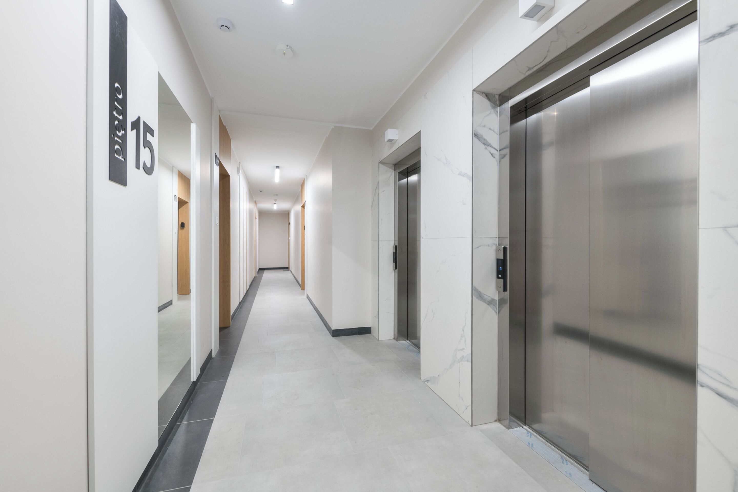 A modern hallway with a marble floor, a number '15' sign, and a stationary elevator.