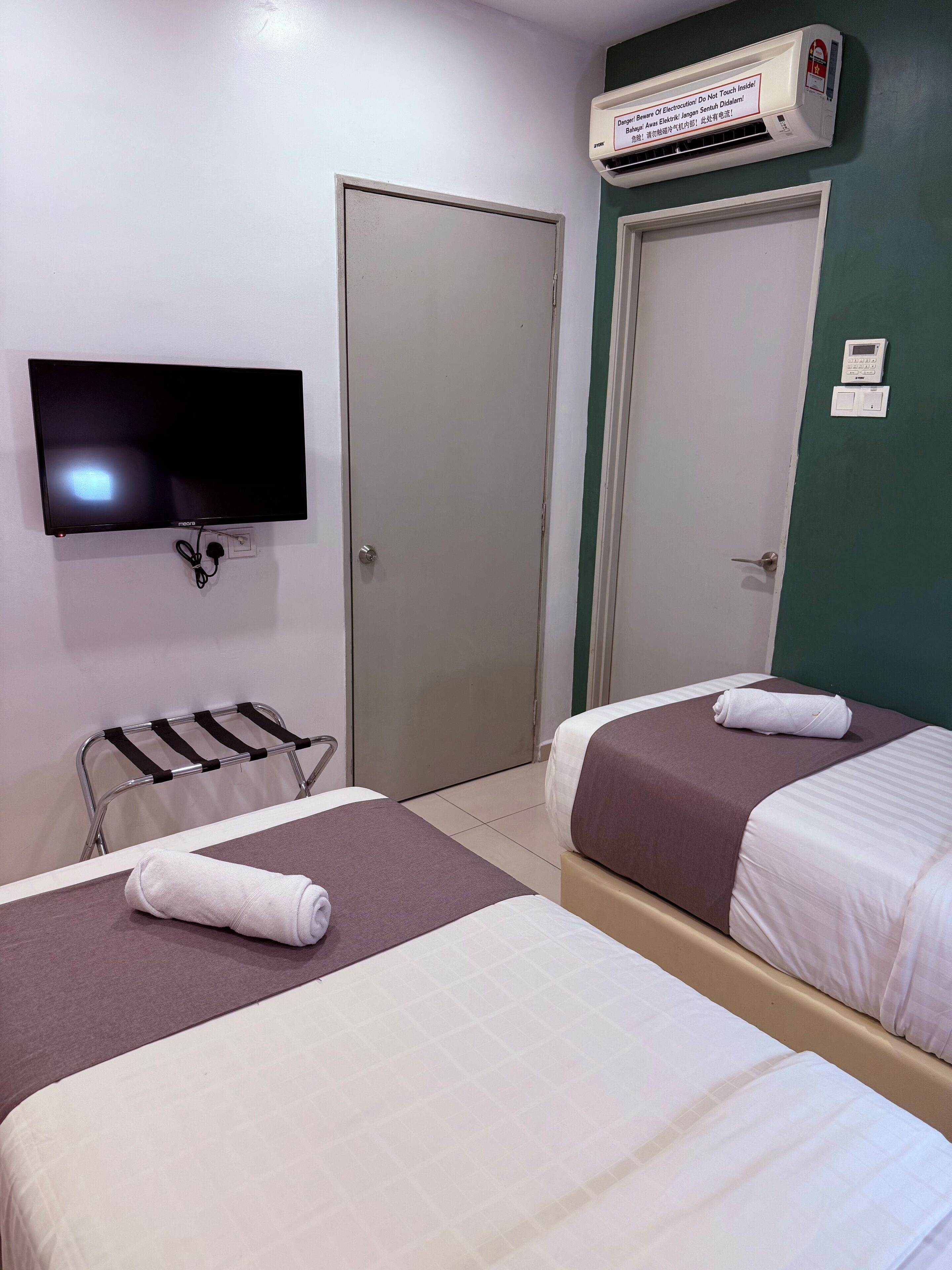 Habitación de hotel con dos camas, un televisor montado en la pared, un equipo de aire acondicionado y una puerta con cerradura de seguridad.
