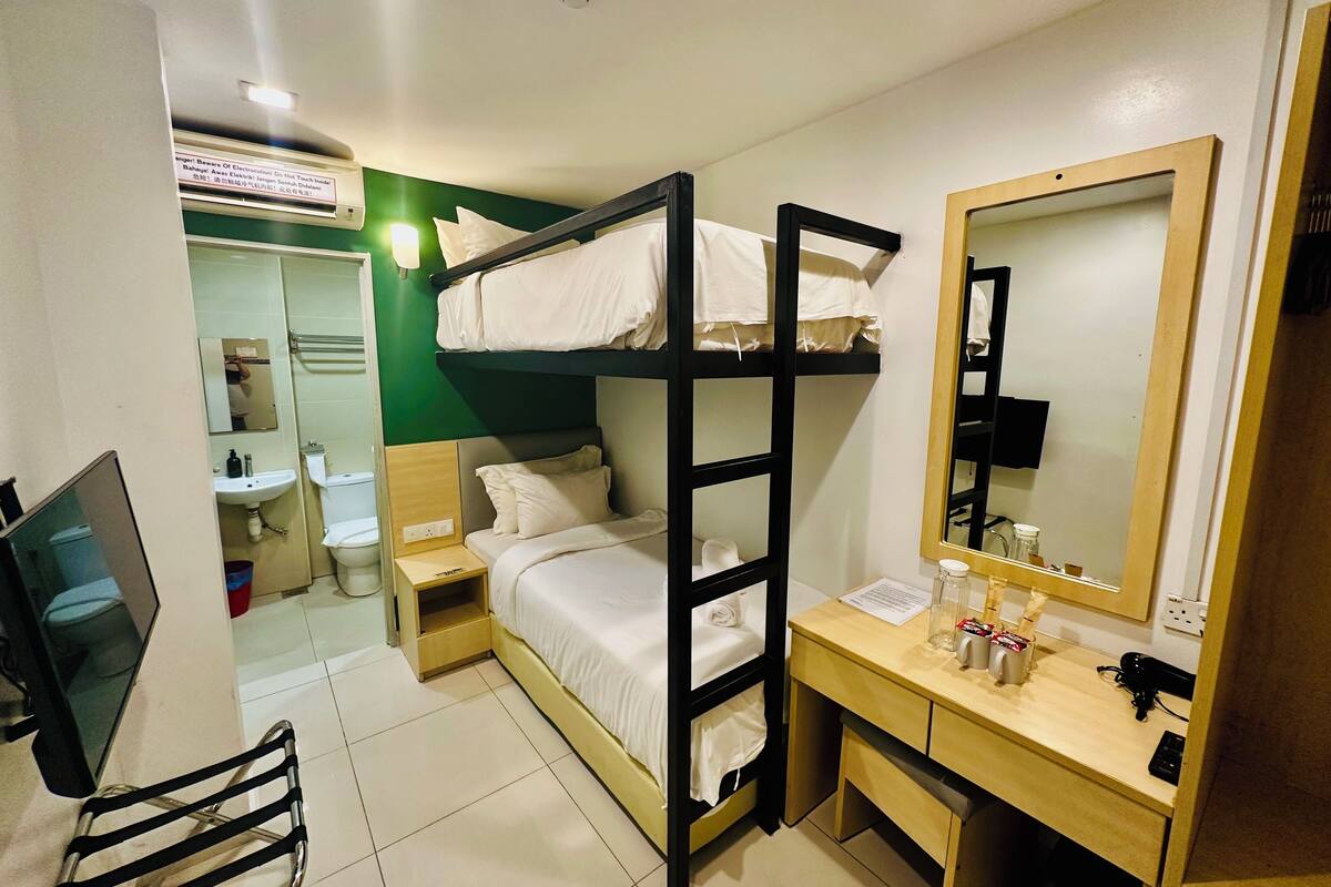A compact hotel room with bunk beds, a small desk, a mirror, and a television.
