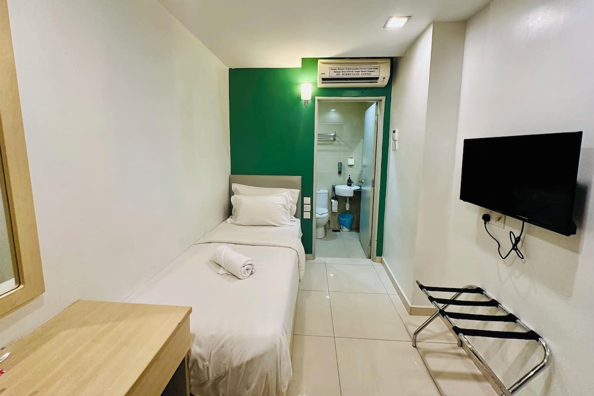 A small hotel room with a bed, a desk, a TV, and a bathroom visible through an open door.