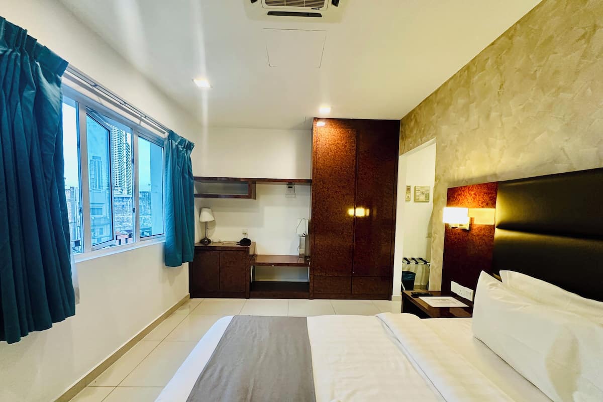 A hotel room with a bed, a desk, a wardrobe, and a view of the city through large windows.