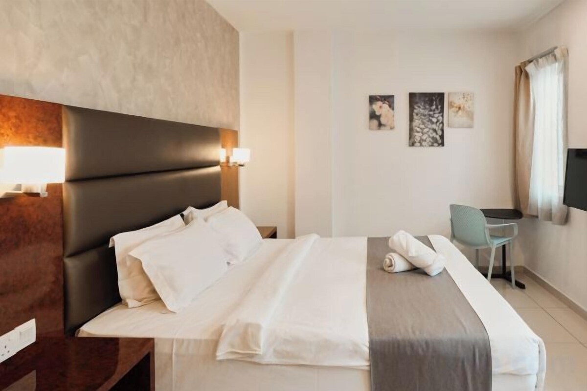A hotel room with a bed, bedside table, lamp, and a desk with a chair.