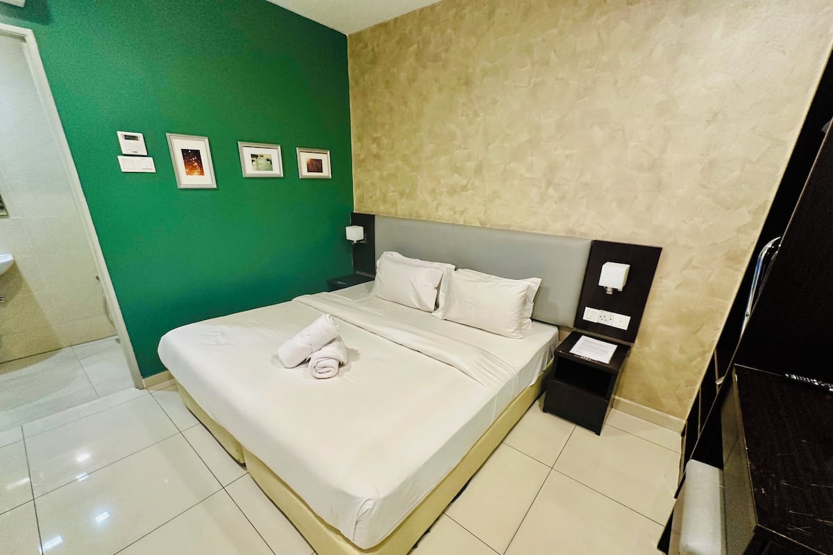 A hotel room with a bed, a nightstand, and a green wall with framed pictures.