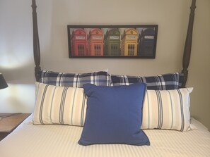 Uma cama com roupa de cama listrada, um travesseiro azul e um quadro com telefones públicos vermelhos na parede.
