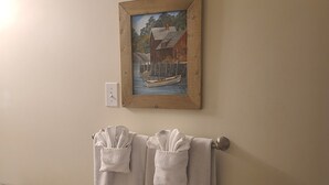 A bathroom with a towel rack holding two towels, a painting of a boat on a dock, and a light switch on the wall. - Elegant & Serene Urban Sanctuary (Halifax)