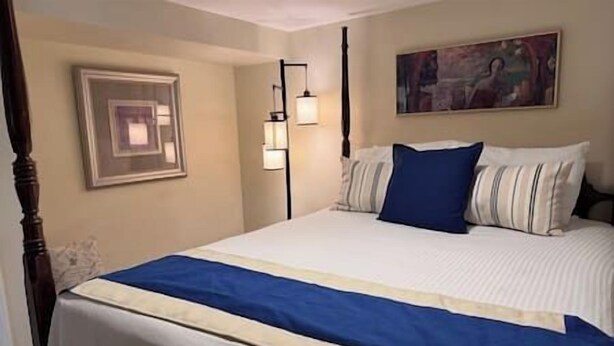 A neatly made bed with a blue and white bedspread, a framed picture on the wall, and a painting above the bed. - Elegant & Serene Urban Sanctuary (Halifax)