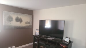 A living room with a flat-screen TV on a black stand, a painting on the wall, and a carpeted floor. - Elegant & Serene Urban Sanctuary (Halifax)