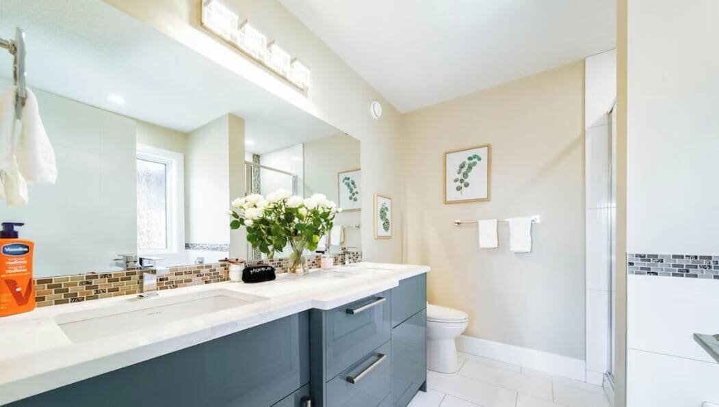 Une salle de bain moderne avec un grand miroir, un lavabo blanc et un meuble-lavabo bleu foncé. On peut voir les toilettes et l’espace de la douche.