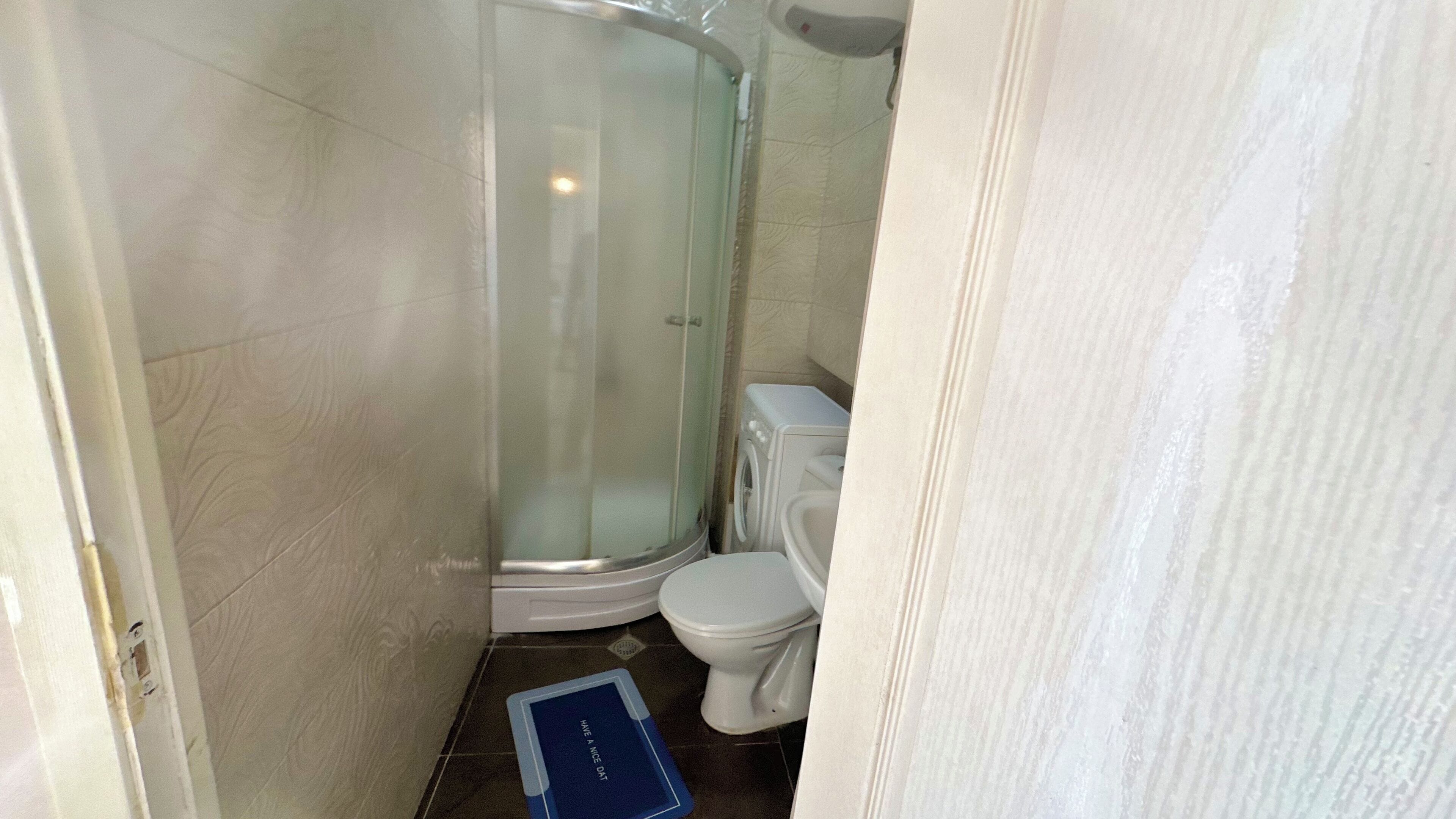 Une petite salle de bain avec une douche à parois de verre, des toilettes et un tapis bleu sur le sol.