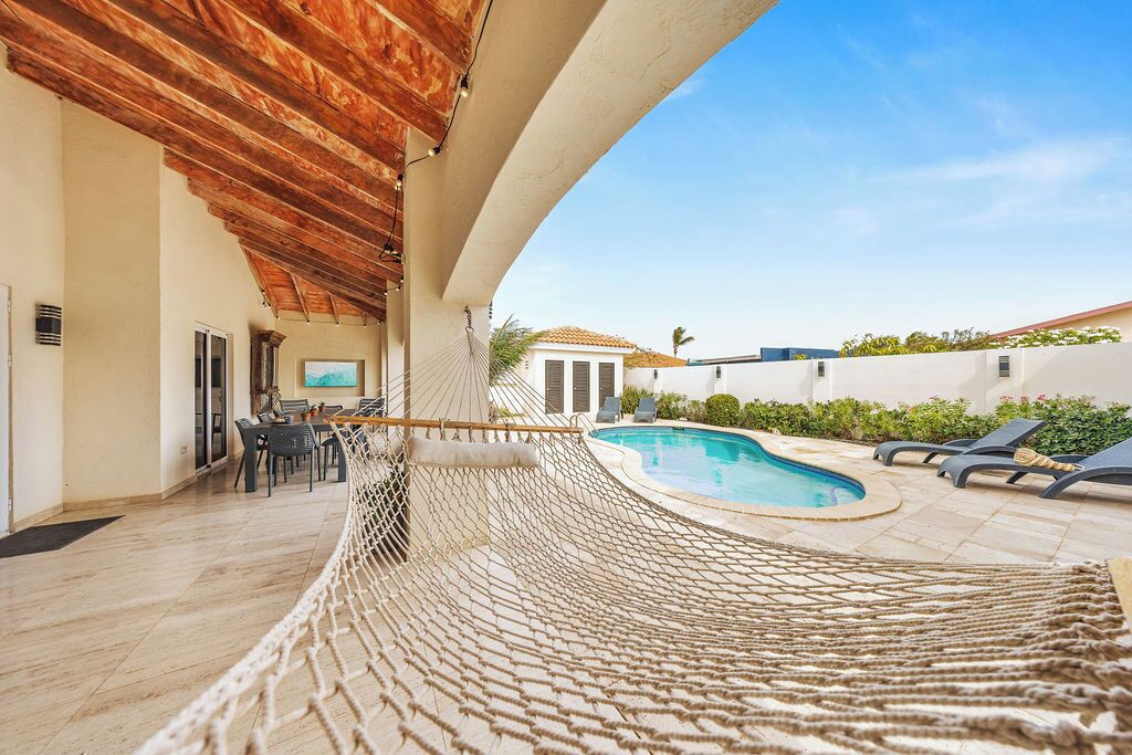 A pool area with a hammock, lounge chairs, and a dining setup.