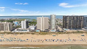Un paisaje urbano costero con rascacielos, una playa de arena con numerosas sombrillas y un puerto deportivo al fondo.